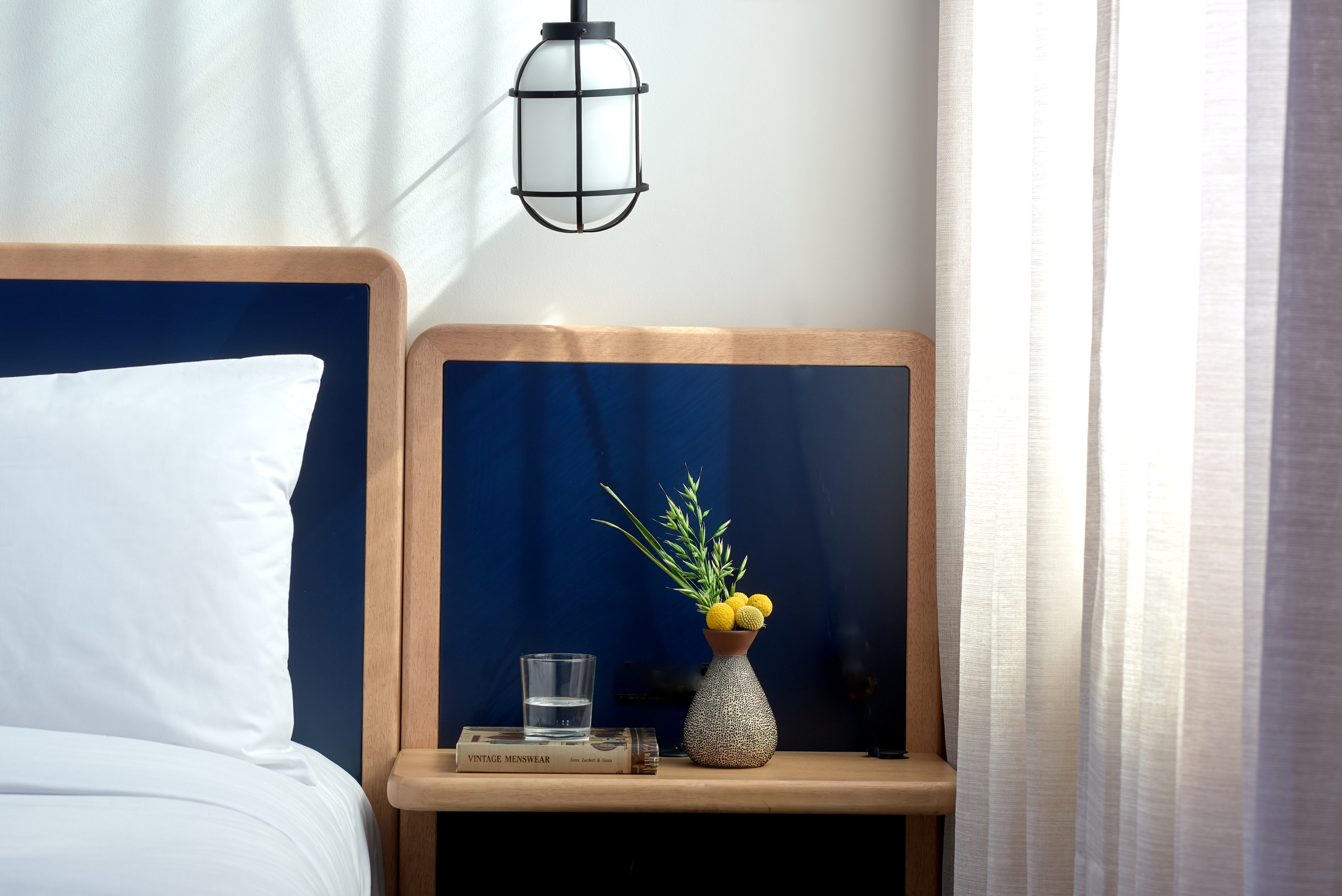 a soft bed with a navy blue headboard and flowers on the nightstand