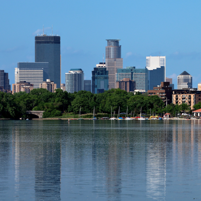 A large lake with a sailboat in the water, large buildings are in the background