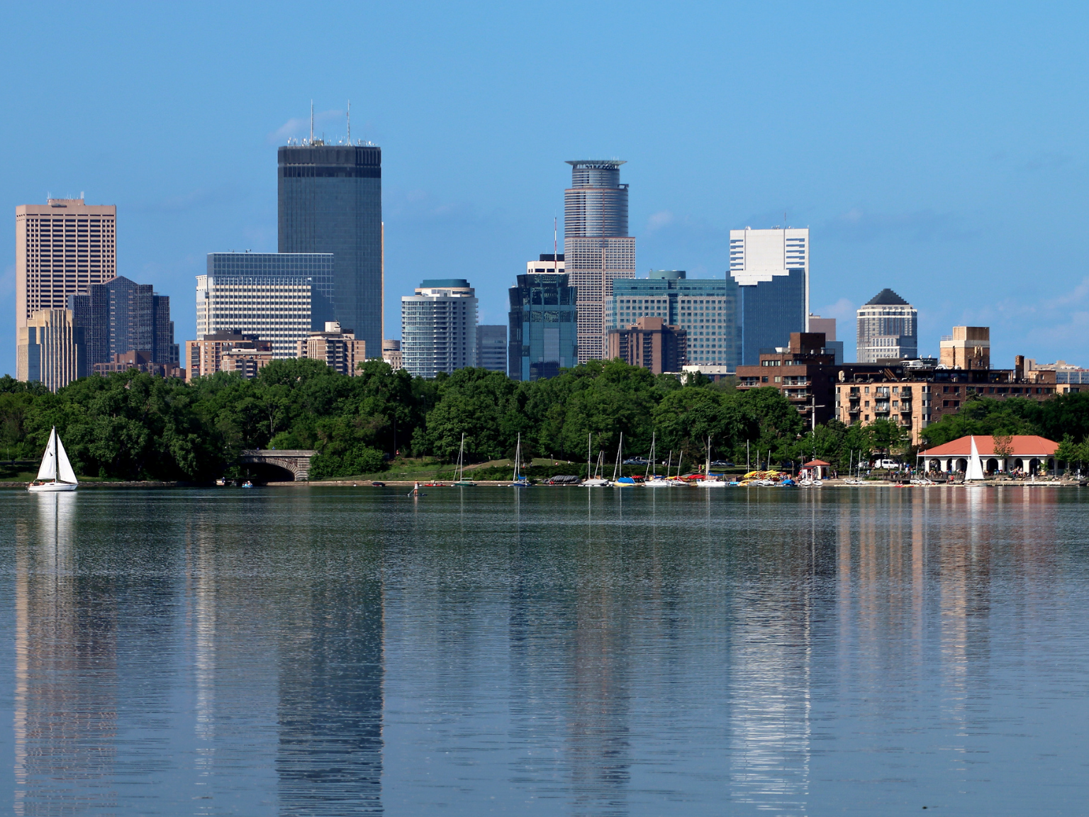 A large lake with a sailboat in the water, large buildings are in the background