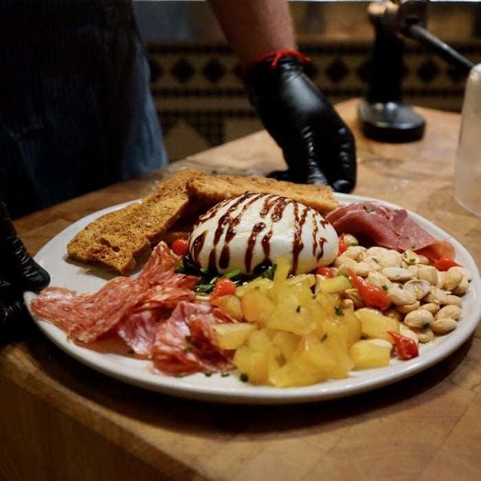 Two hands wearing gloves holding plate of mozzarella and accompaniments